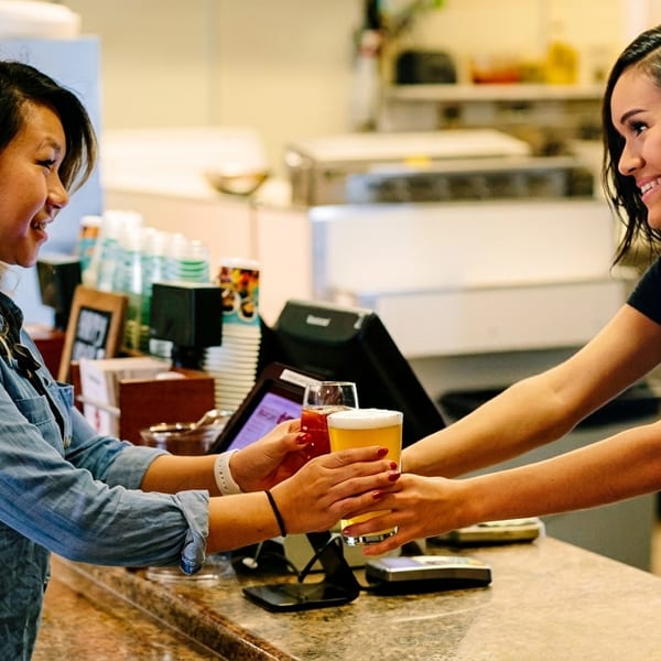 A bartender hands a customer a glass of beer and a cocktail across a bar.