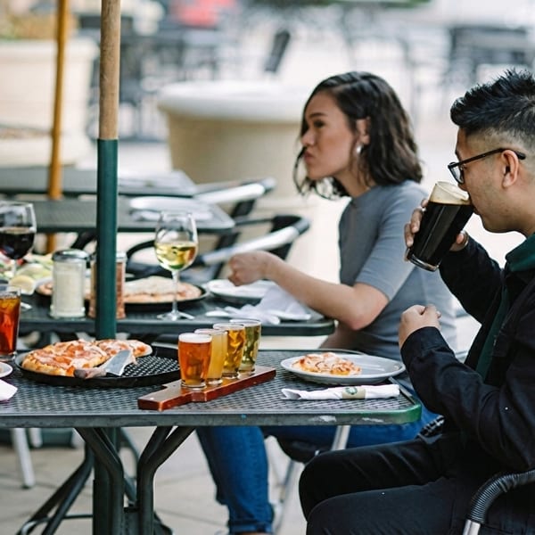 Two people enjoying pizza and drinks at an outdoor restaurant patio table.