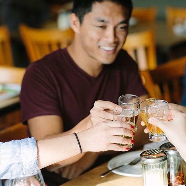 Friends clinking glasses of beer and cider at a restaurant table, smiling and enjoying themselves.