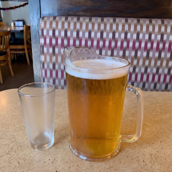 A pitcher of beer and a frosted glass on a restaurant table with patterned booth seating.